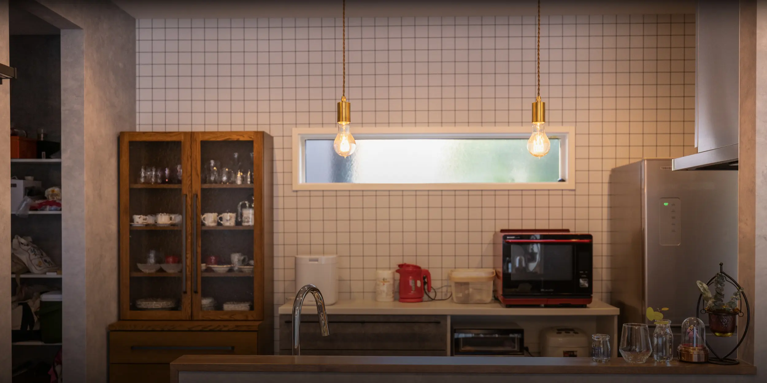 横浜の工務店による注文住宅：タイル張りの壁と木製家具、照明が特徴的なおしゃれなキッチン